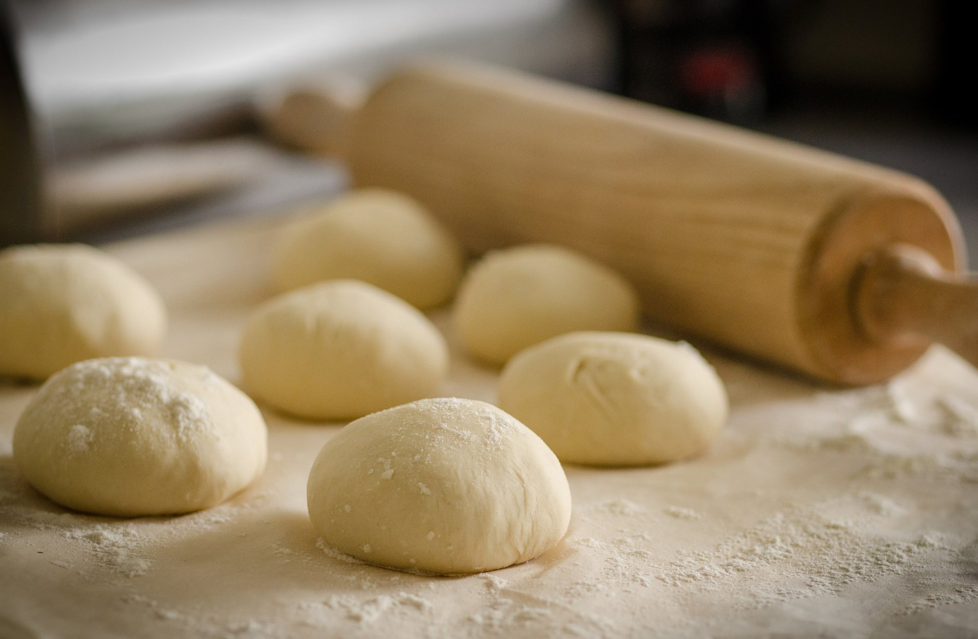 Des pâtons qui reposent sur un plan fariné, un rouleau à pâtisserie à côté
