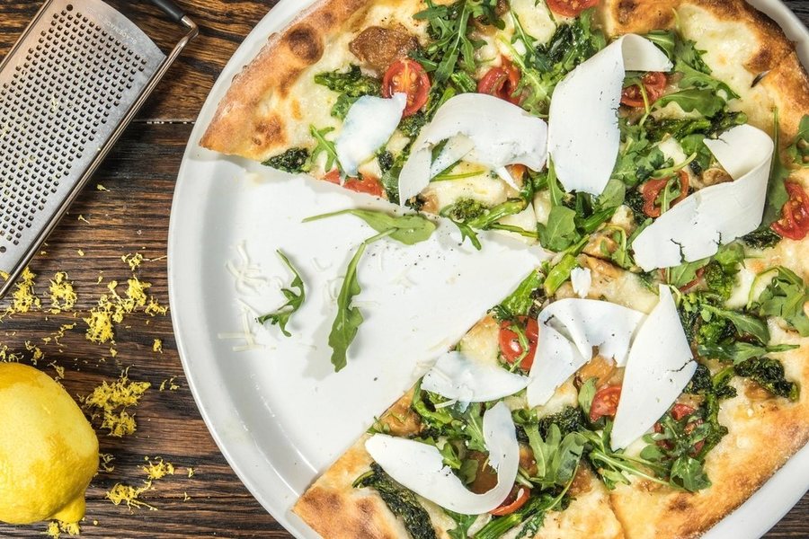 Une pizza blanche à la roquette et aux copeaux de parmesan, un citron à côté