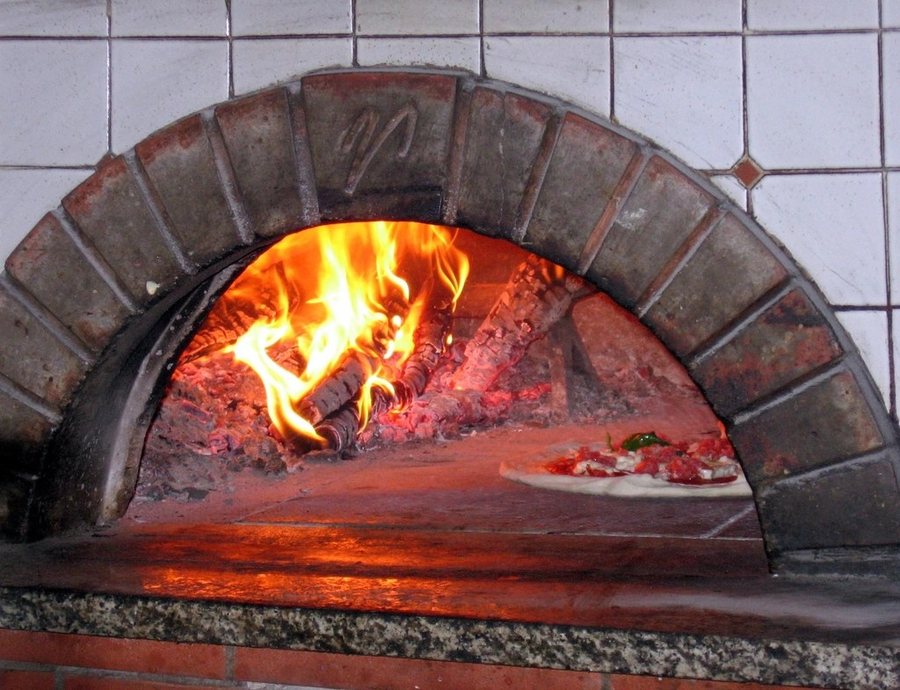 La bouche voûtée d’un four à bois, les flammes au fond, une pizza qui cuit