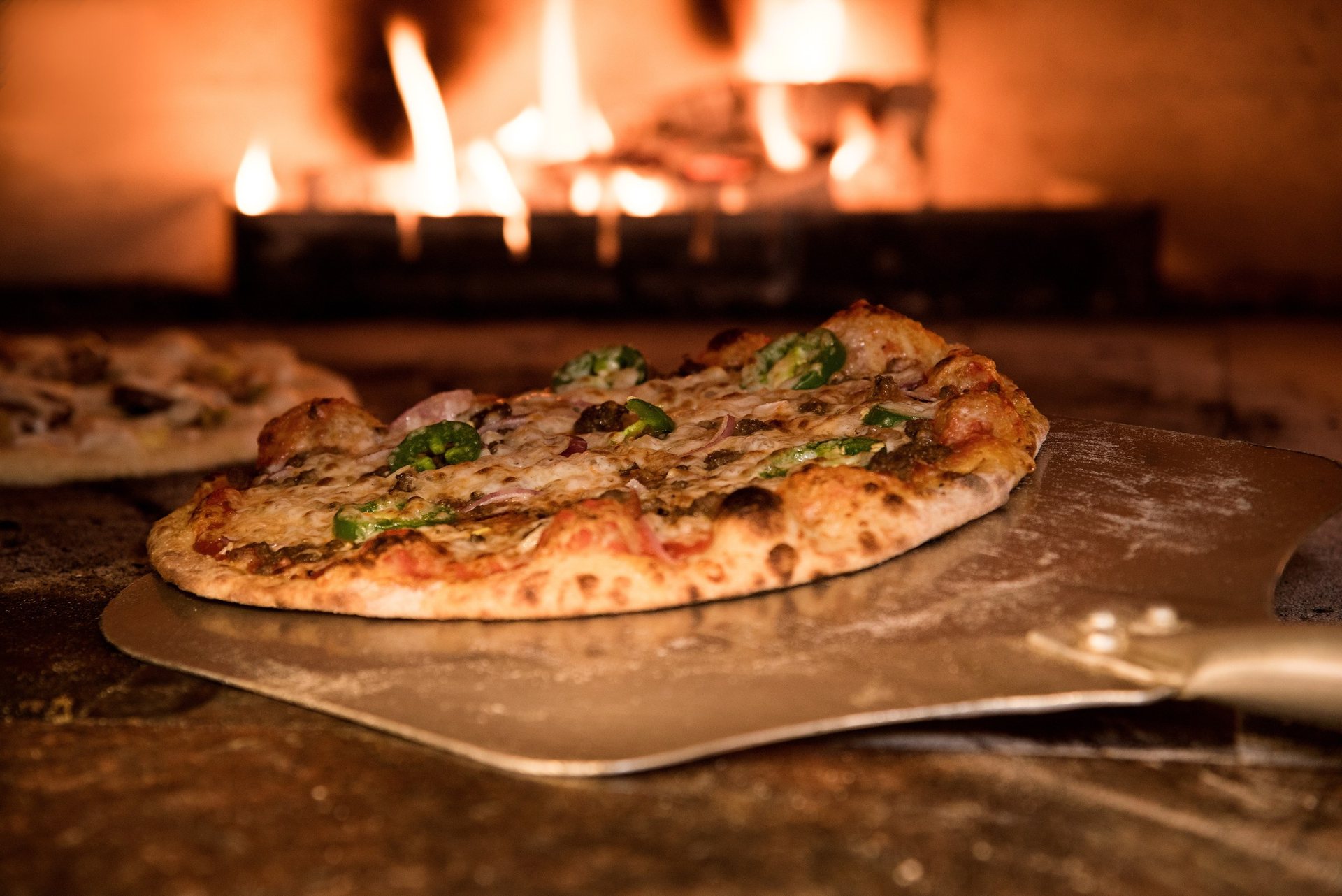 Une pizza sur la pelle, devant les flammes du four à bois