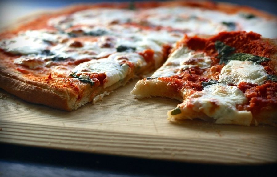Une pizza margherita entamée, mozzarella fondue et basilic, sur une planche
