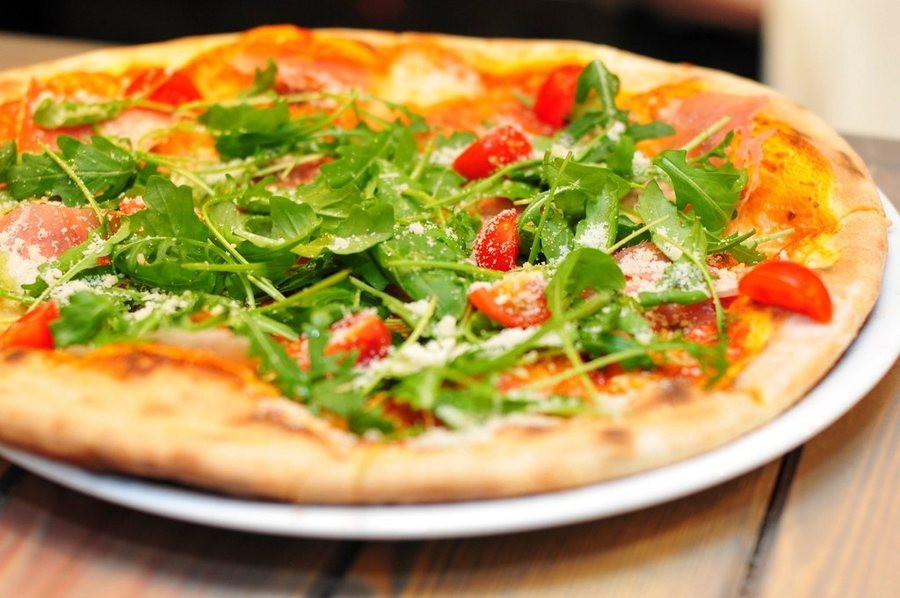 Une pizza au jambon cru, couverte de roquette et de tomates cerises