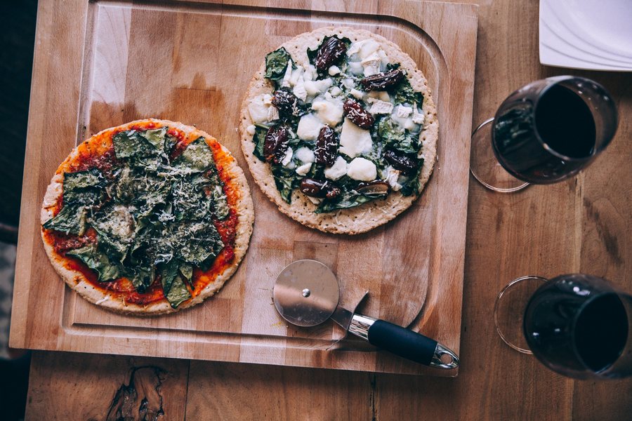 Deux pizzas sur une planche, une roulette et deux verres de vin rouge
