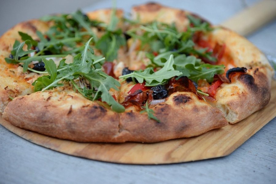 Une pizza à la roquette et aux olives noires sur une pelle en bois
