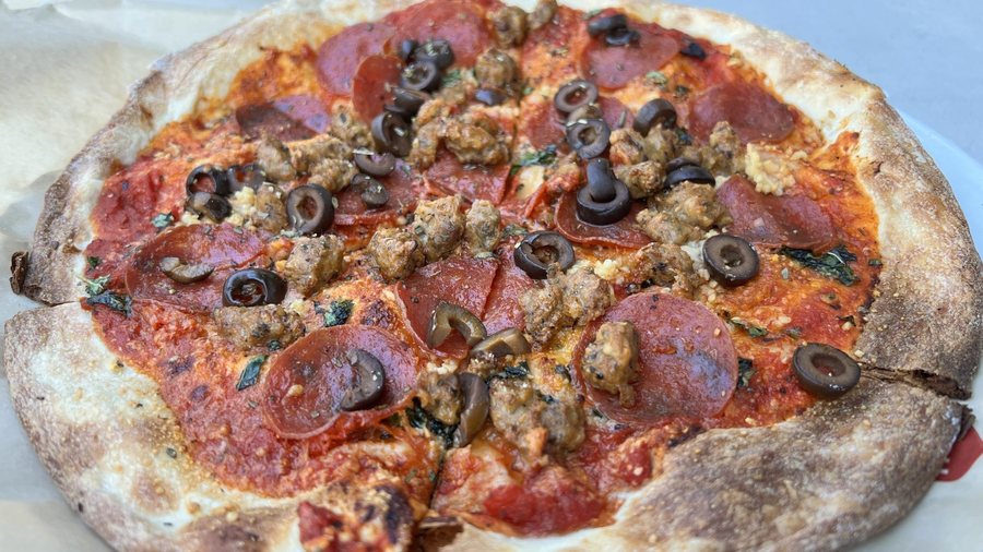 Une pizza à pâte fine, saucisse émiettée, salami et olives noires